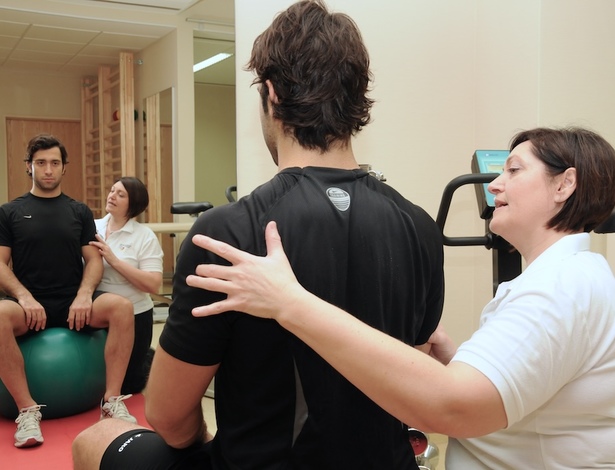 Physiotherapeutin mit Patient, der auf einem Sitzball sitzt.